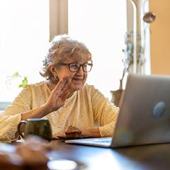 Older woman, waving at someone through her computer in an online meeting ie Zoom. 