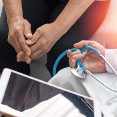 Elderly patient sitting with doctor who is holding tablet and stethoscope
